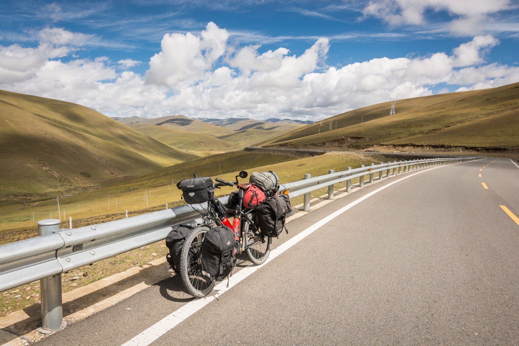 My loaded touring bicycle on an empty road high on the Tibetan plateau, mountains behind