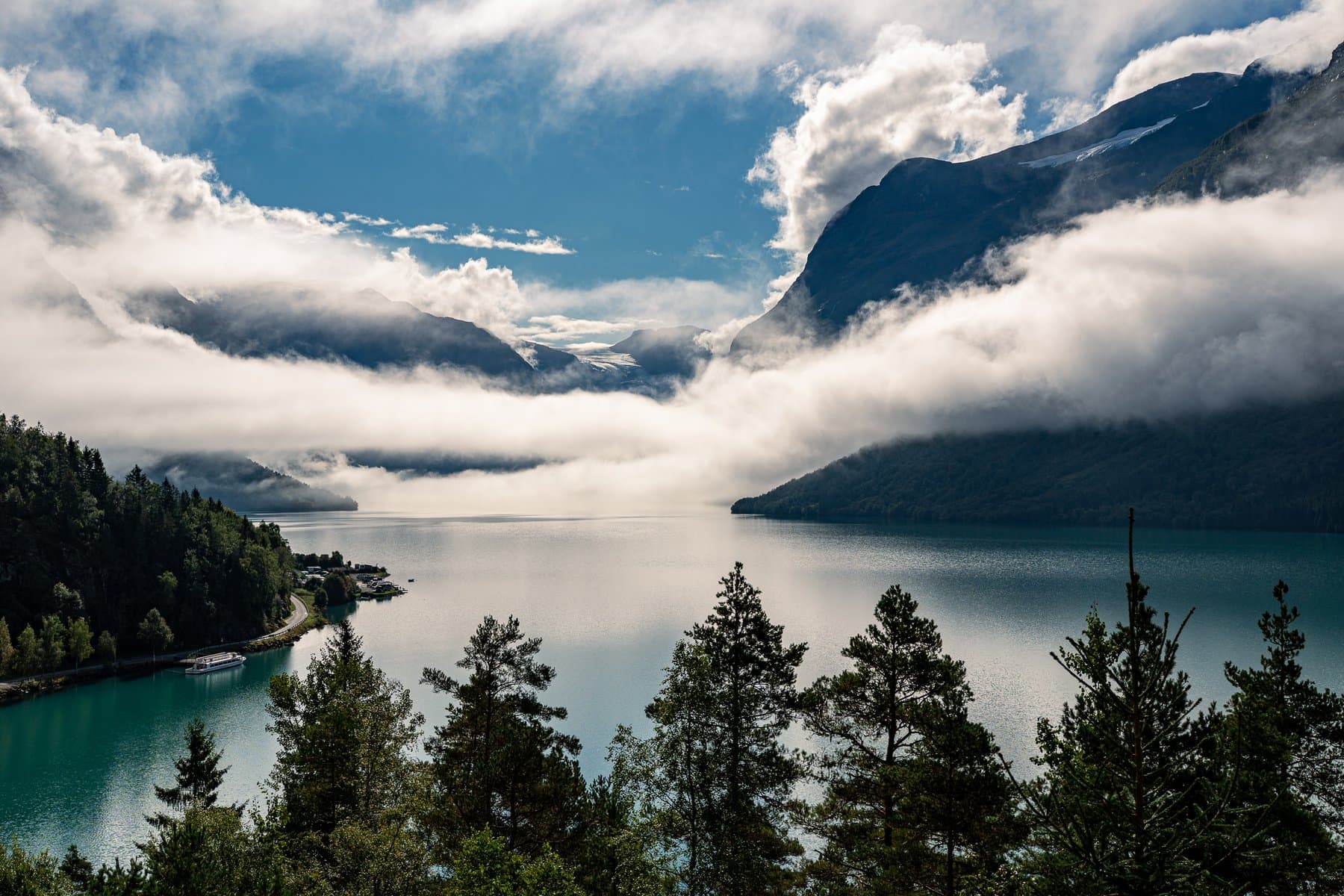A turquoise fjord lake below steep mountains, with low cloud spilling down the valley
