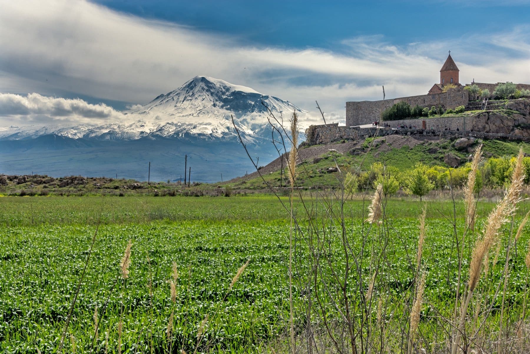 Snow-capped Mount Ararat rising behind green fields and a hilltop monastery
