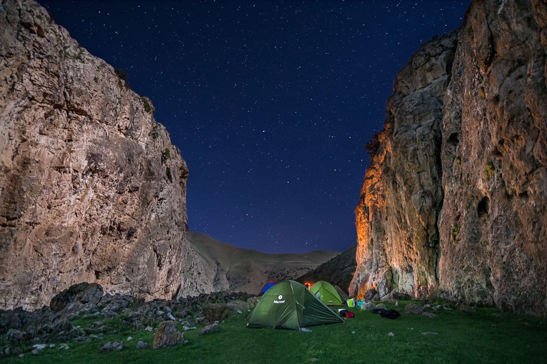 My tent lit up at night between canyon walls under a field of stars