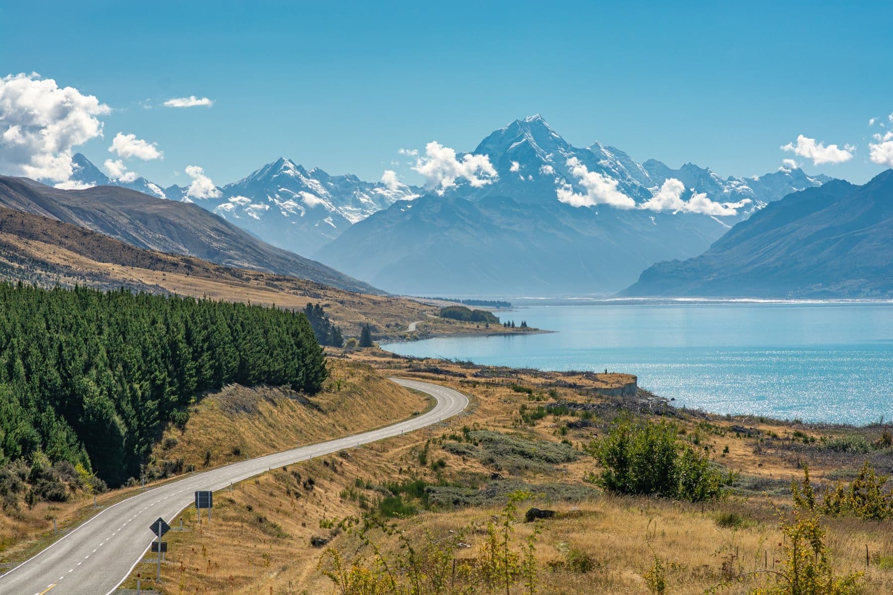 A road running beside a glacial-blue lake beneath the snows of Aoraki / Mount Cook